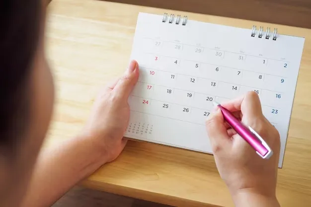 pagina-calendario-mano-femenina-sosteniendo-pluma-sobre-mesa-escritorio_293060-6710